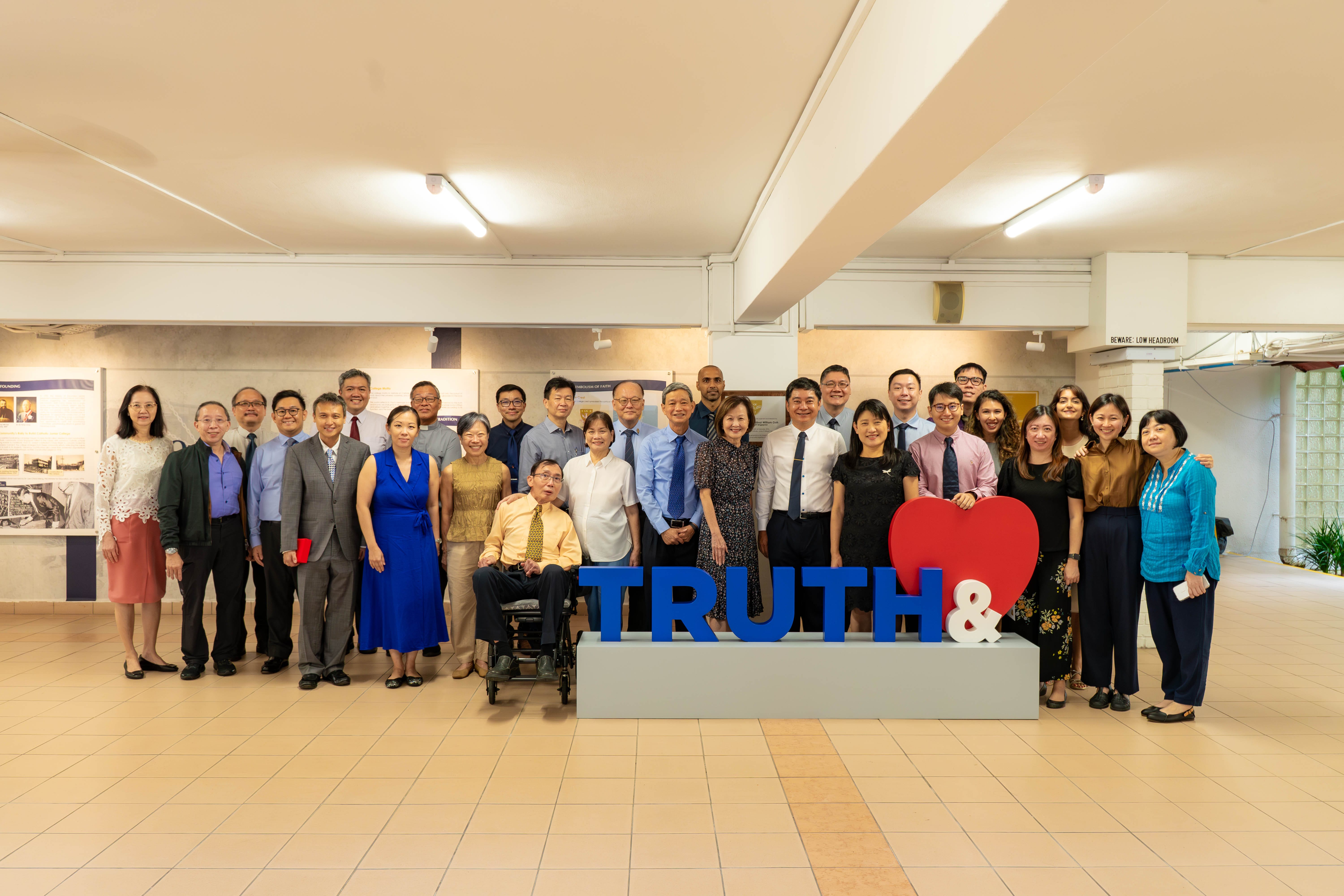 A large group of people posing indoors behind a sign reading TRUTH& with a red heart symbol.